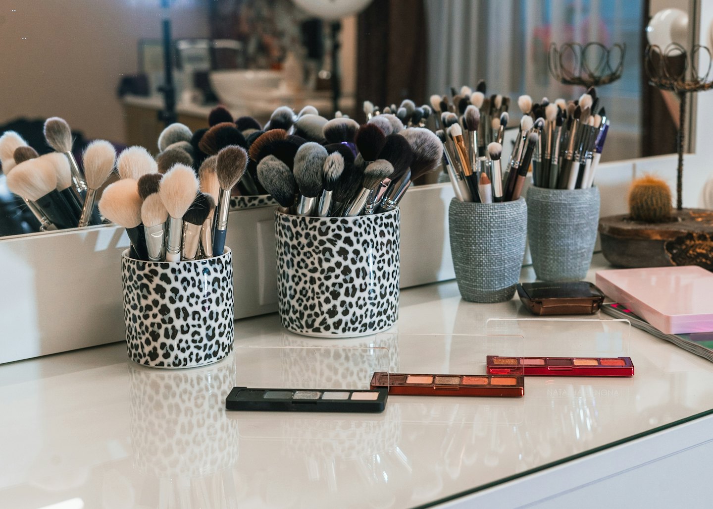 Makeup brushes neatly arranged in leopard print and grey holders on a vanity.